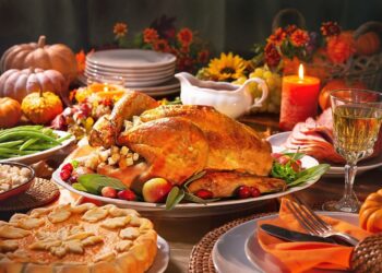 Thanksgiving dinner. Roasted turkey garnished with cranberries on a rustic style table decoraded with pumpkins, vegetables, pie, flowers, and candles