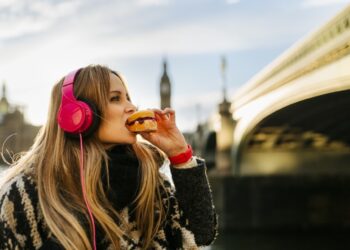 UK, London, young woman listening music and taking a snack near Westminster Bridge