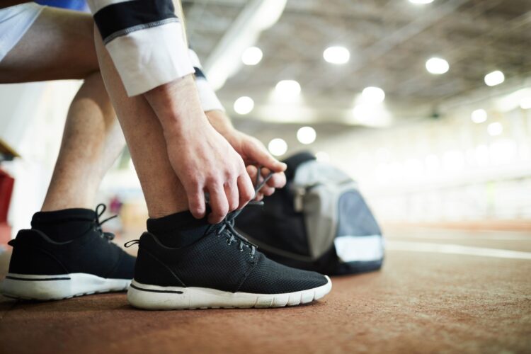 Contemporary sportsman tying shoelaces on sneakers while preparing for training at stadium